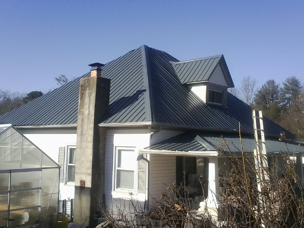 Dark blue standing seam metal roof on a white farmhouse with dormer — Slate & Tile Roof Repair by Roofing Brothers in Woodman