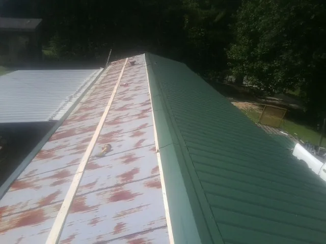 Old rusted panels beside newly installed green metal roofing — Wind Damage Roof Repair by Roofing Brothers in Woodman