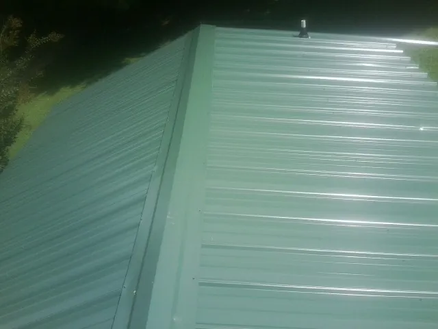 New green metal panels meeting at the ridge of a roof — Flat Roof Repair work by our crew in Woodman