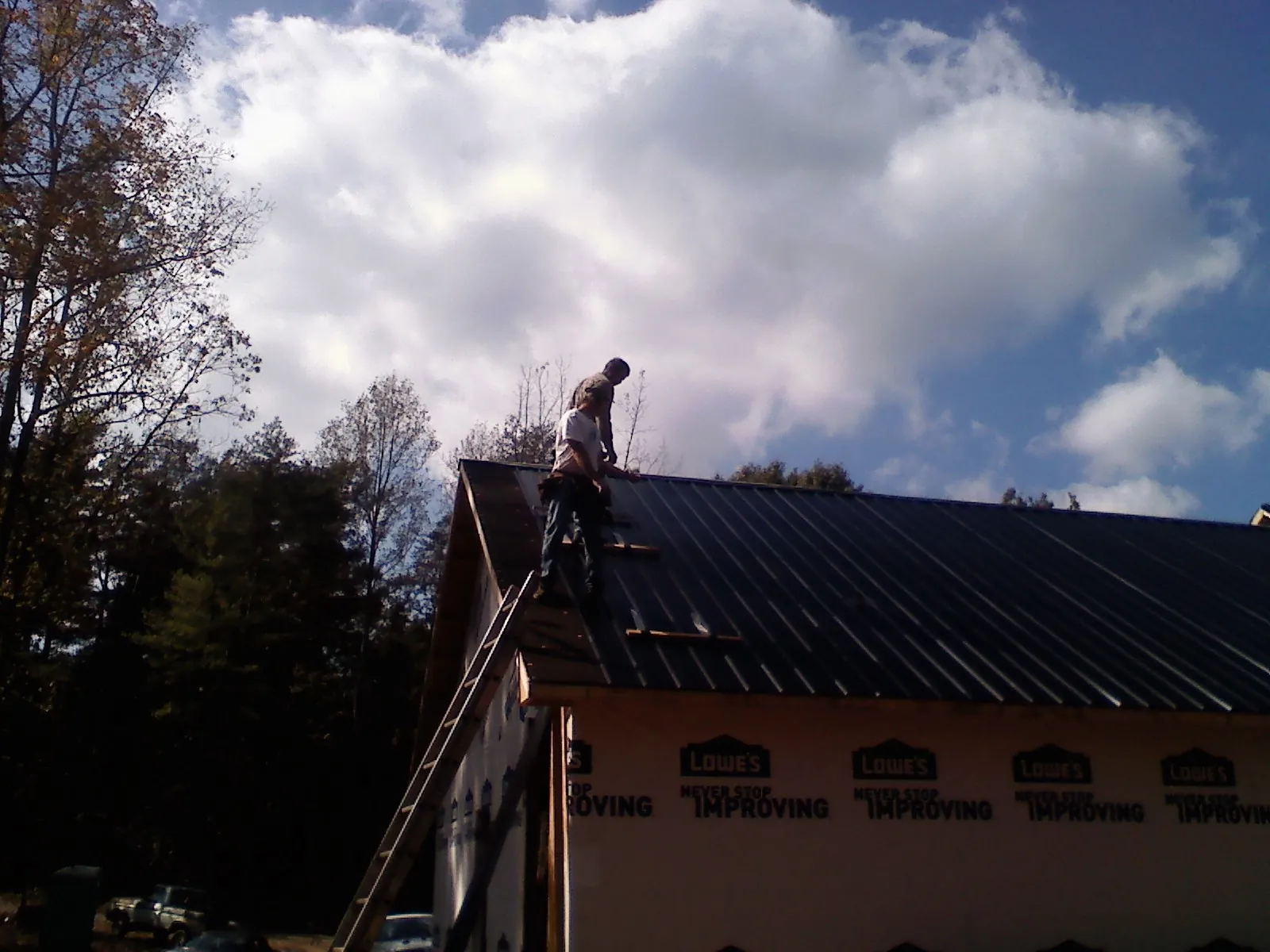 Roofer fastening dark metal panels high against a cloudy sky, from a Roof Inspection job in Woodman