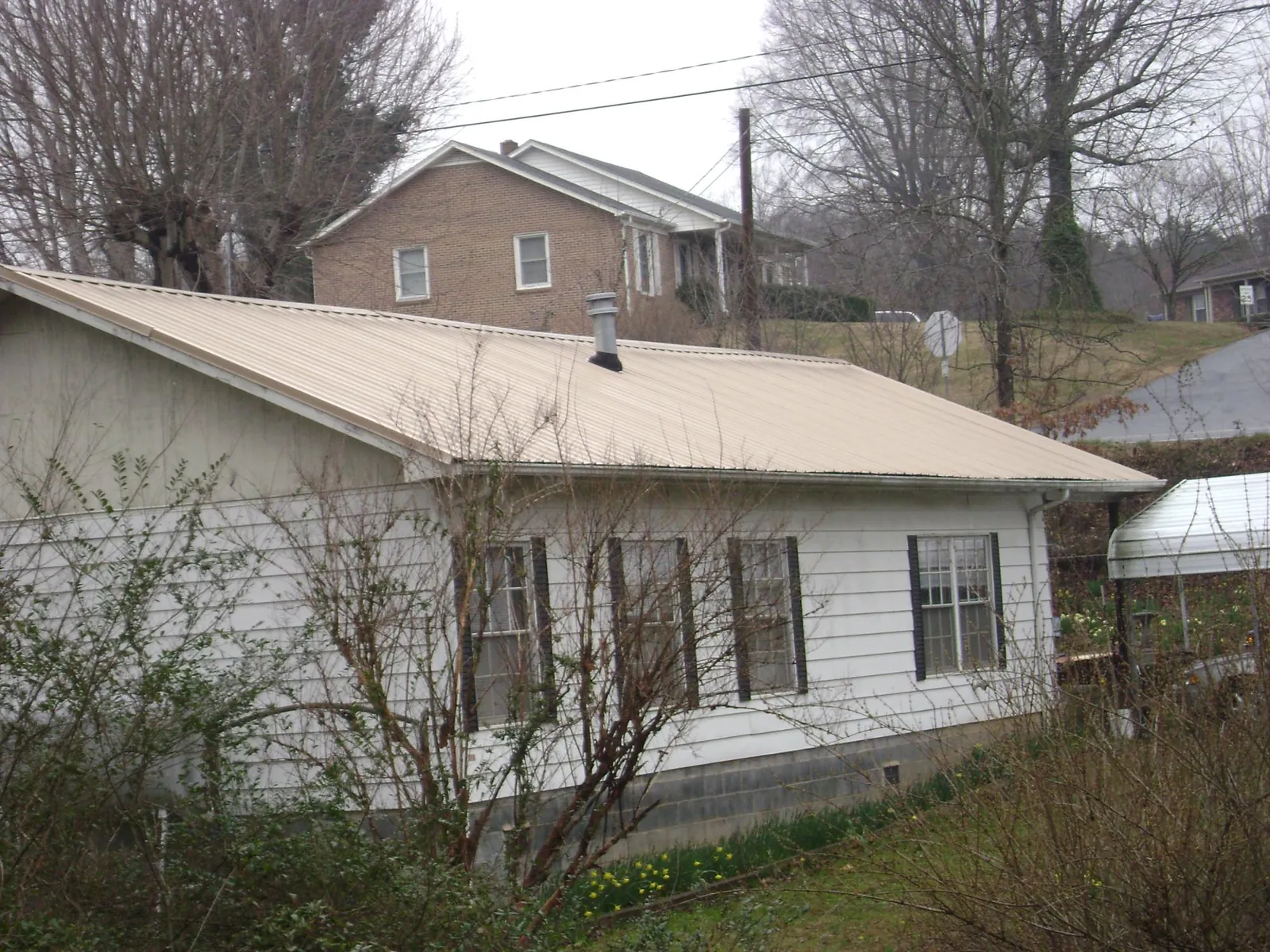 Tan metal roof on a white sided house set into a hillside — Commercial Roofing by Roofing Brothers in Woodman