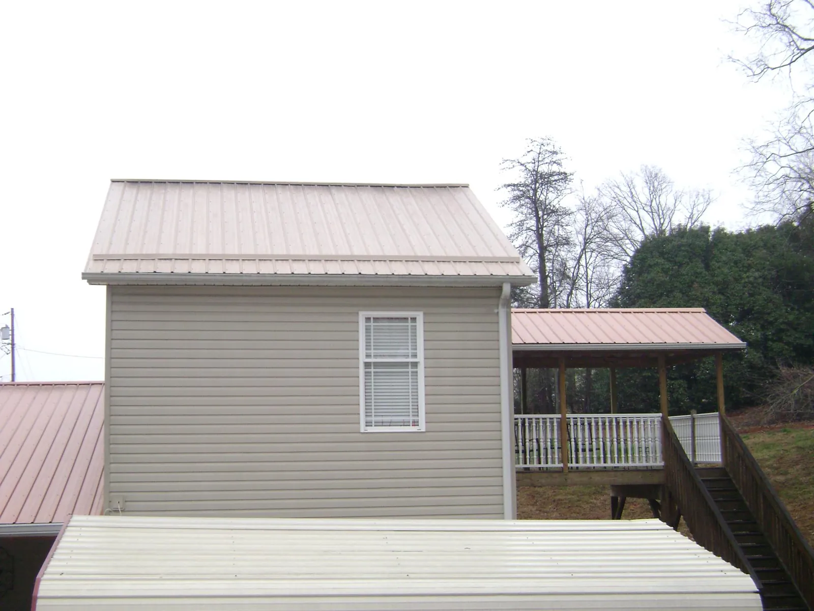 Tan metal roofs on a two story addition and attached porch, from a Roof Replacement job in Woodman